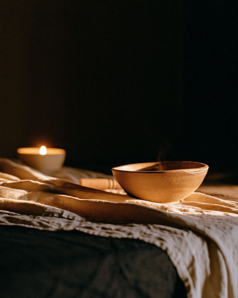 A singing bowl and a candle on linen in a darkened room.
