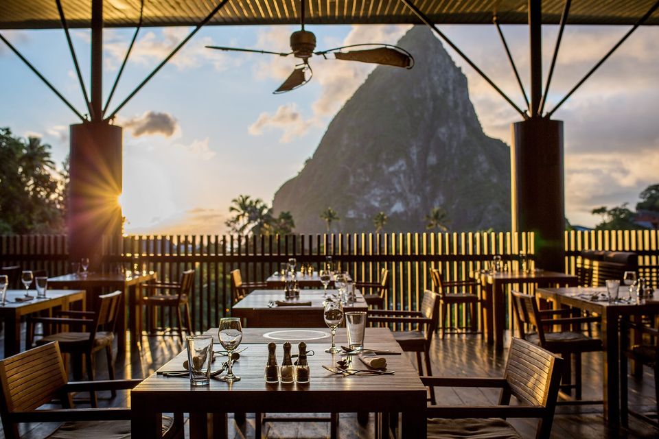 A terrace table set for dinner with the Pitons beyond at golden hour.